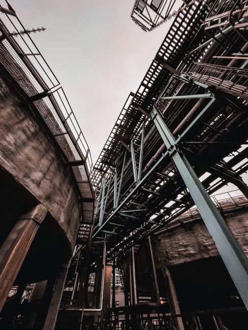 A striking upward view of industrial steel structures under a cloudy sky, showcasing architectural intricacy.
